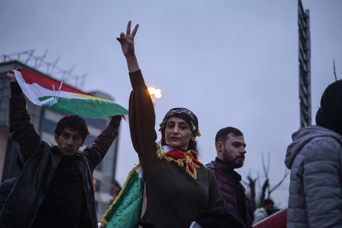Una manifestante alza la mano e mostra un segno di pace vicino a una persona che tiene una bandiera