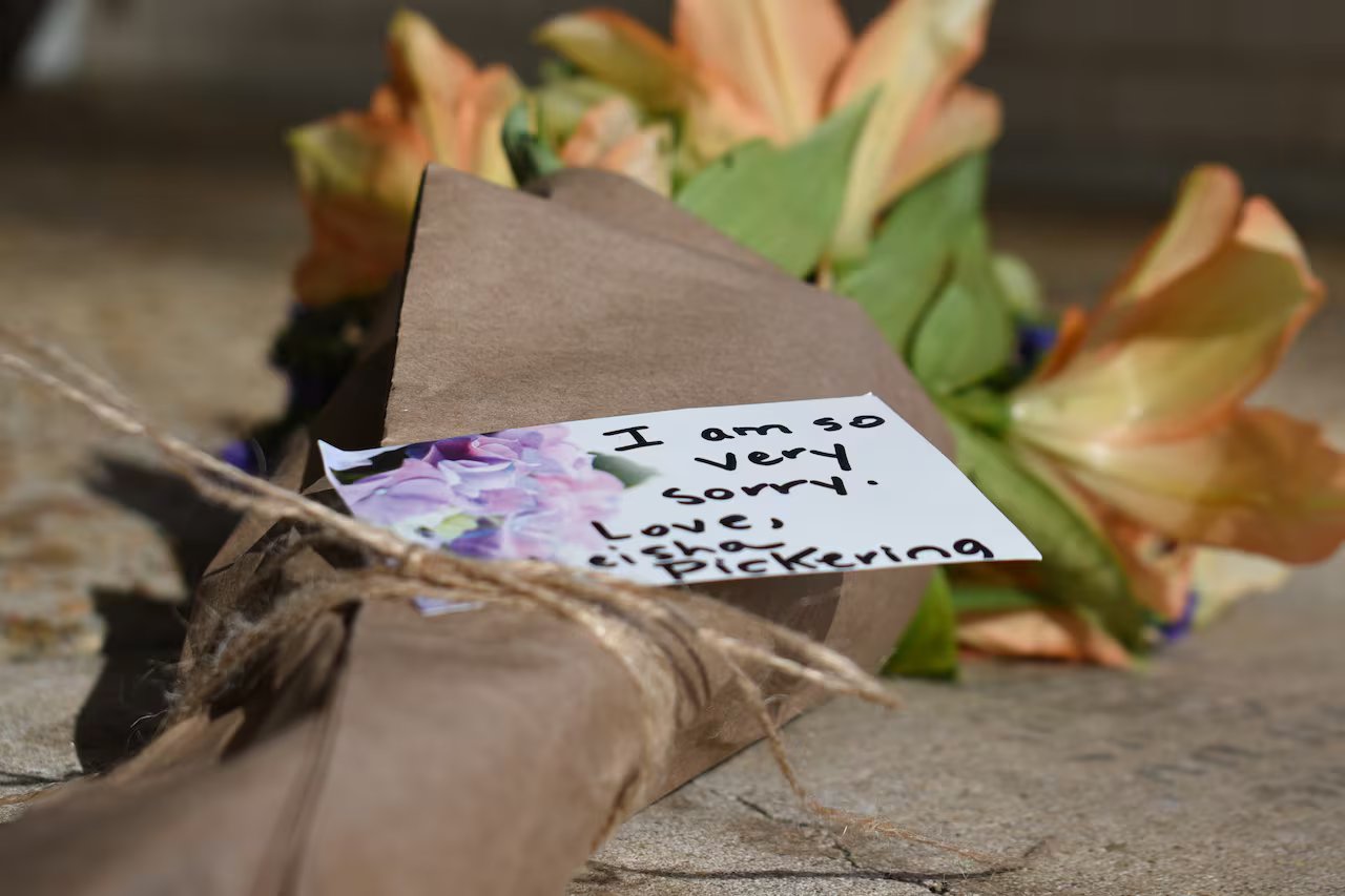 Sul pavimento giace un mazzo di fiori con allegato un biglietto.