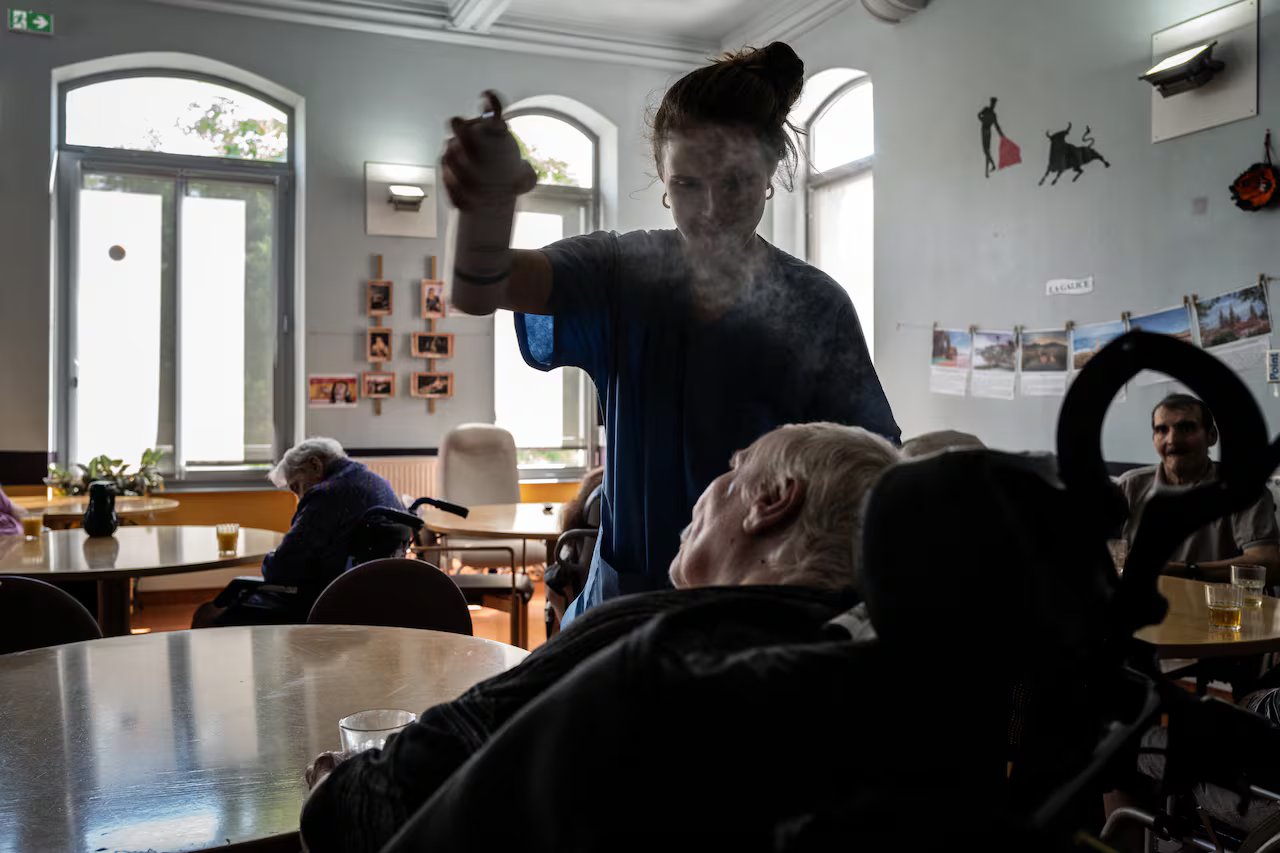 Una donna spruzza acqua su una persona anziana che dorme su una sedia a rotelle meccanica in una calda giornata a Lione, in Francia.