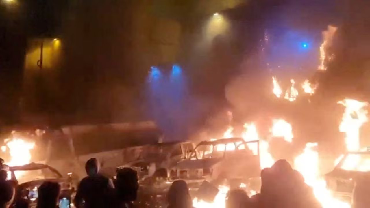 In questo screenshot ottenuto da un video sui social media pubblicato il 9 gennaio 2026, i manifestanti si riuniscono mentre i veicoli bruciano, nel mezzo di disordini antigovernativi, a Teheran, in Iran.