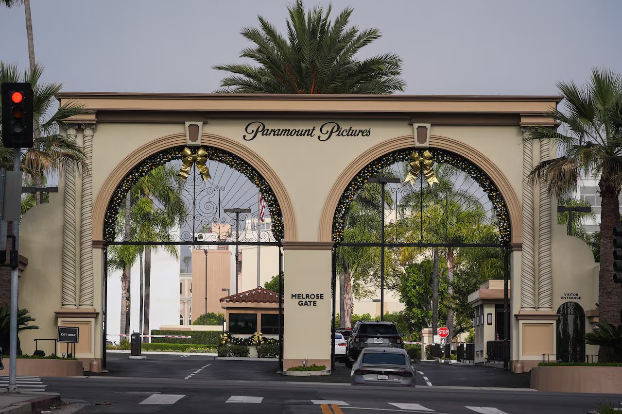 Sono mostrate due auto che attraversano un cancello a doppio arco. Il cancello è circondato da palme.