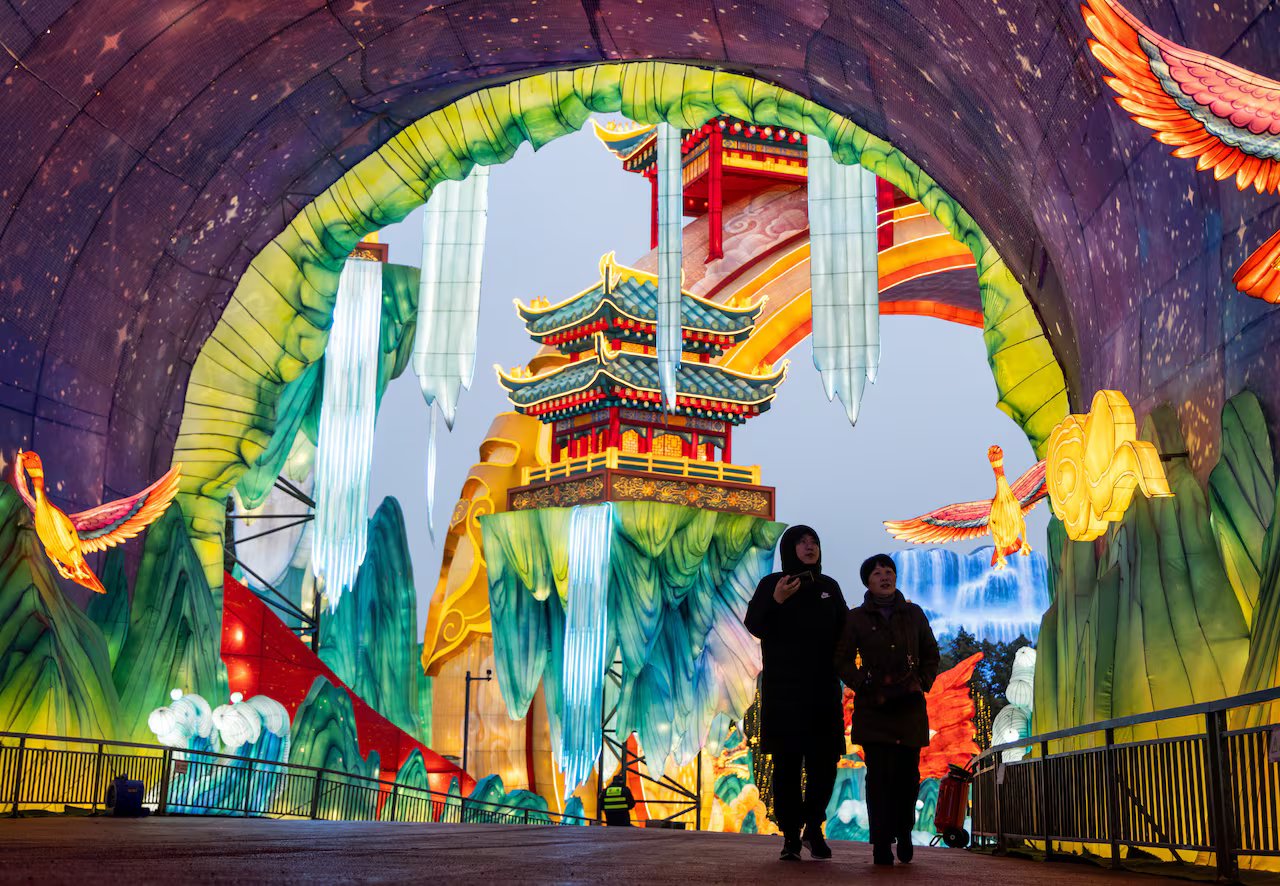 Due persone camminano attraverso un tunnel all'interno di un'installazione luminosa con una gigantesca lanterna colorata a forma di tempio, che viene illuminata di notte.