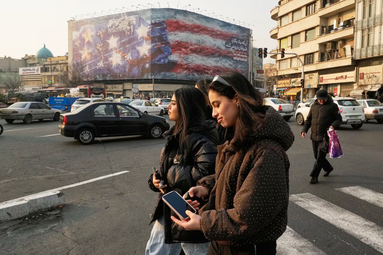 Due giovani donne camminano lungo una strada urbana accanto a un cartellone pubblicitario di una portaerei con sopra la bandiera a stelle e strisce