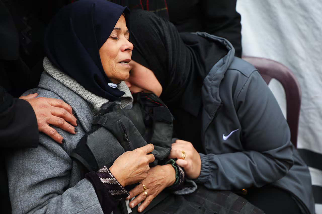 Due donne che indossano un copricapo con gli occhi chiusi si confortano a vicenda.