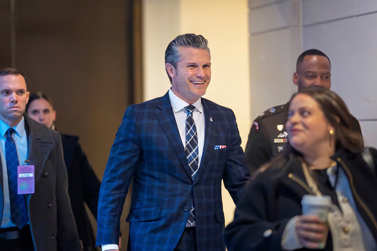 Un uomo dai capelli grigi sorride felicemente mentre cammina con un abito scozzese blu. Una donna che cammina davanti a lui lo guarda e sorride mentre tiene in mano il caffè.