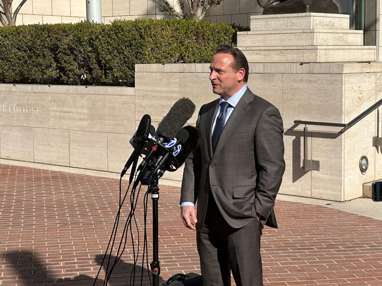 Un uomo in giacca e cravatta parla ai microfoni davanti all'aula del tribunale