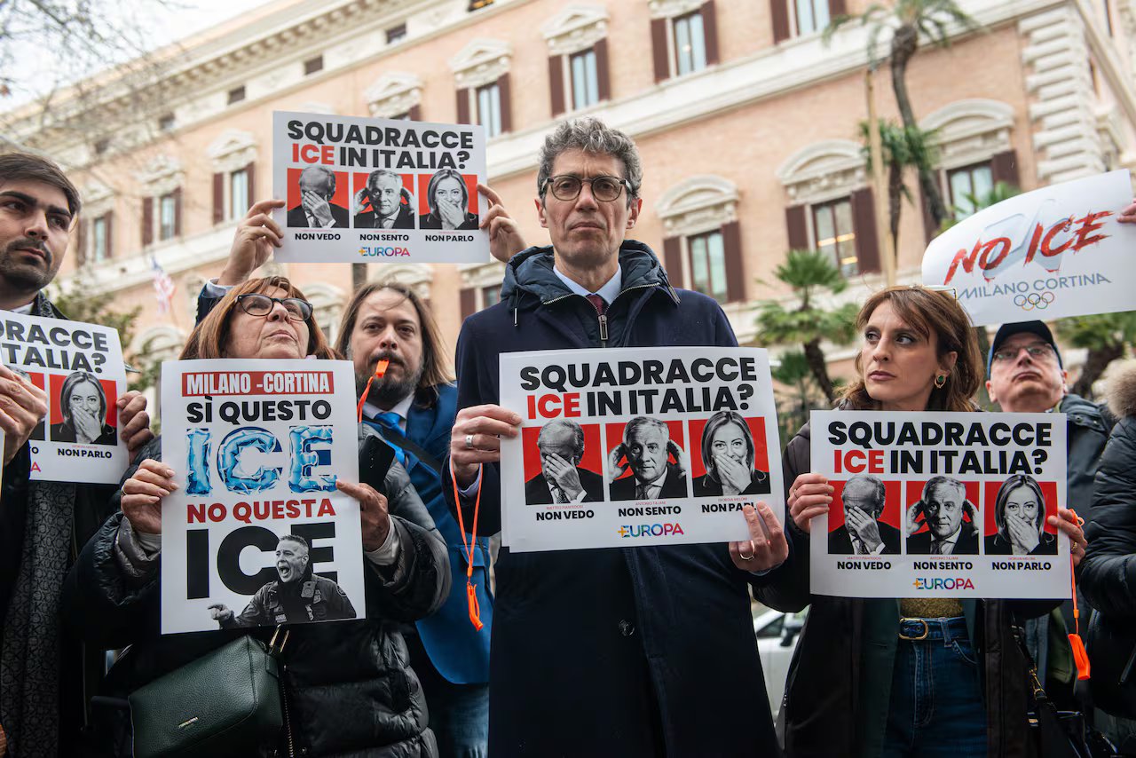Un gruppo di persone in piedi davanti a un grande edificio dalla facciata in pietra con cartelli in italiano