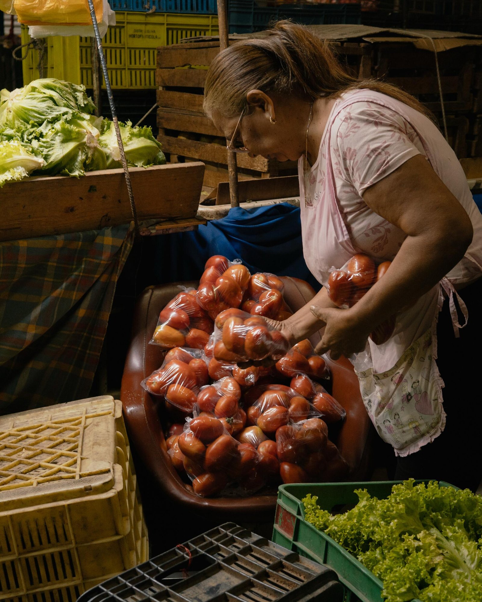 Una donna organizza sacchi di pomodori vicino a contenitori di plastica contenenti prodotti verdi 