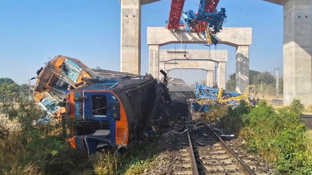 Un vagone passeggeri deragliato giace su un lato accanto al binario ferroviario.