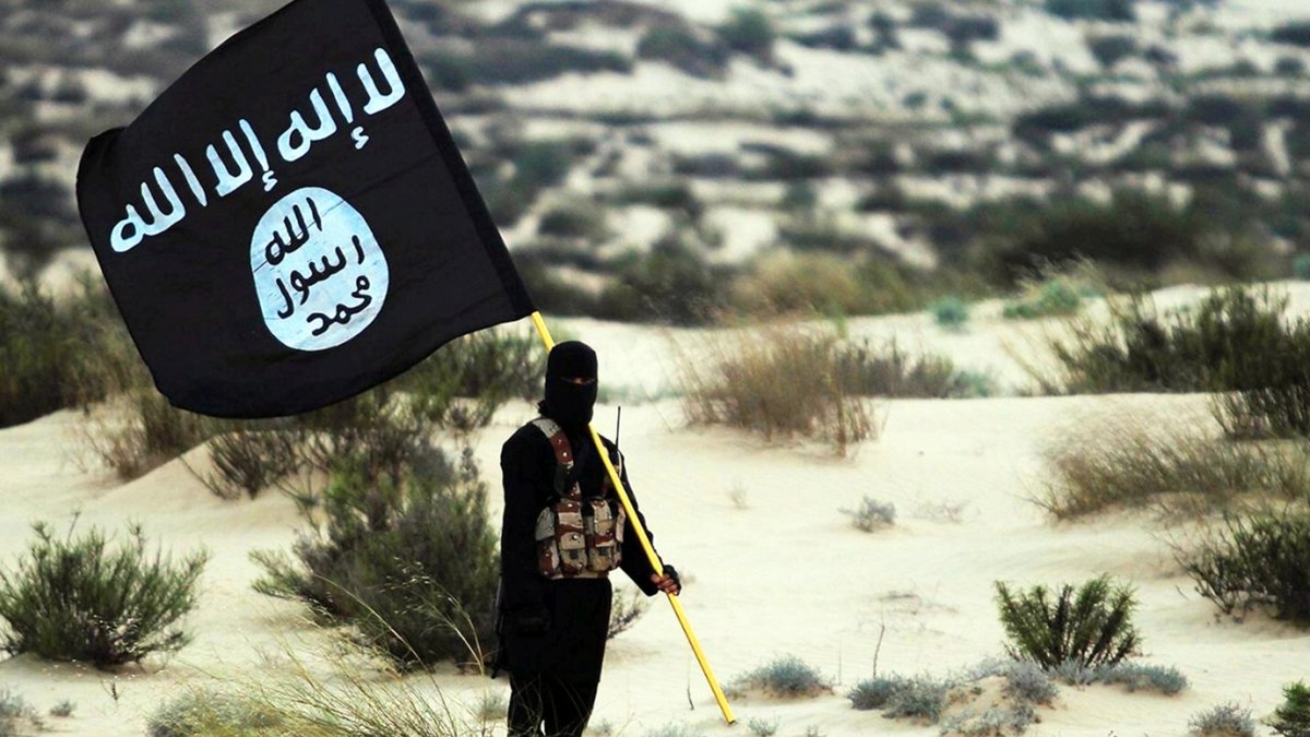 Un combattente dell'Isis tiene in mano una bandiera dell'Isis in un'area desertica