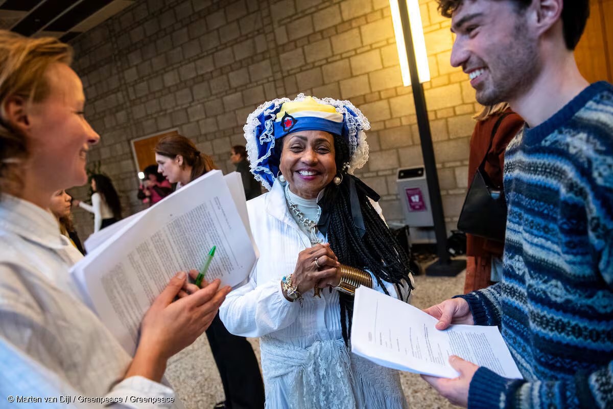 Una donna che indossa un cappello con volant sorride tra due persone che tengono dei documenti